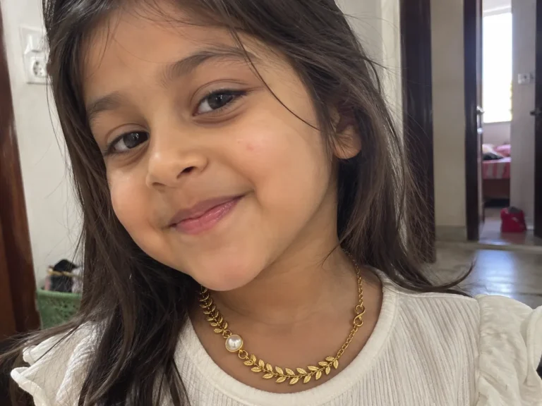 Little girl smiling at home, dressed up in the ANIKI Tiny Pearl, Golden Leaves Neck Piece